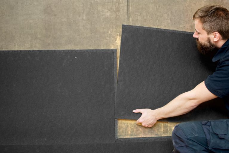 Eine Person installiert schwarze Platten an einer Wand aus Holz.